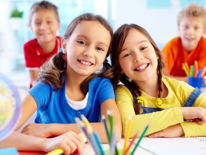 Portrait of two diligent girls looking at camera at workplace with schoolboys on background